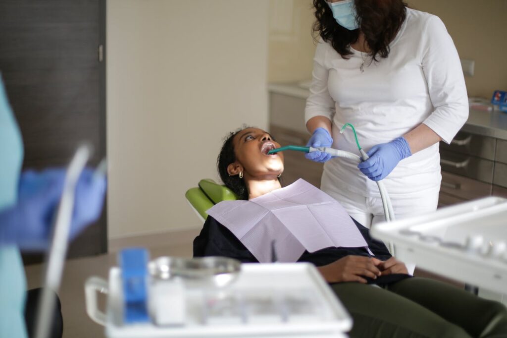 Crop female assistant fixing filling of teeth of African American woman with opened mouth while crop dentist preparing material